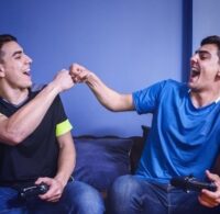Två vänner spelar konsol tillsammans i soffan och gör en fist bump
