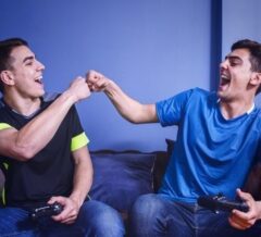 Två vänner spelar konsol tillsammans i soffan och gör en fist bump