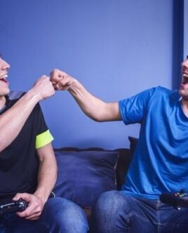 Två vänner spelar konsol tillsammans i soffan och gör en fist bump