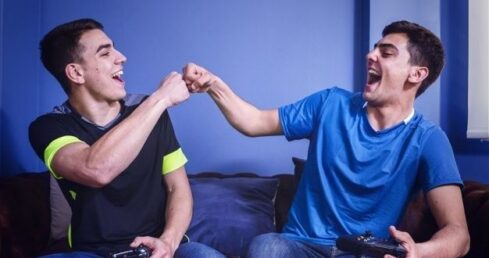 Två vänner spelar konsol tillsammans i soffan och gör en fist bump