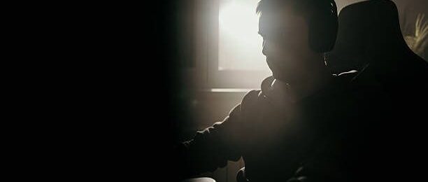 Silhuett av spelare med hörlurar framför en skärm i mörkt rum