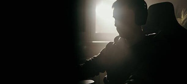 Silhuett av spelare med hörlurar framför en skärm i mörkt rum